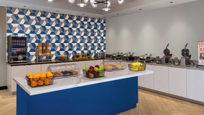 A breakfast bar with a geometric patterned wall, a coffee machine, and various food items. - Fairfield Inn & Suites By Marriott Norfolk (Norfolk)