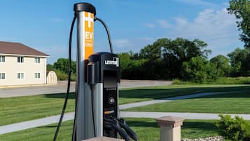 An EV charging station branded with 'LEVITON' and 'EV CHARGING ONLY' in a suburban setting with a house and greenery in the background.