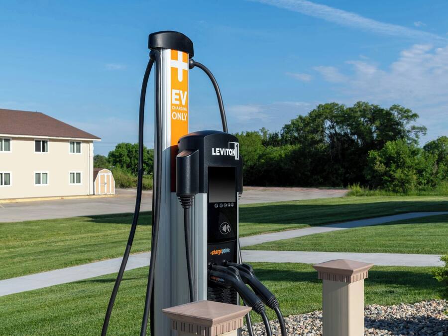 An EV charging station branded with 'LEVITON' and 'EV CHARGING ONLY' in a suburban setting with a house and greenery in the background.