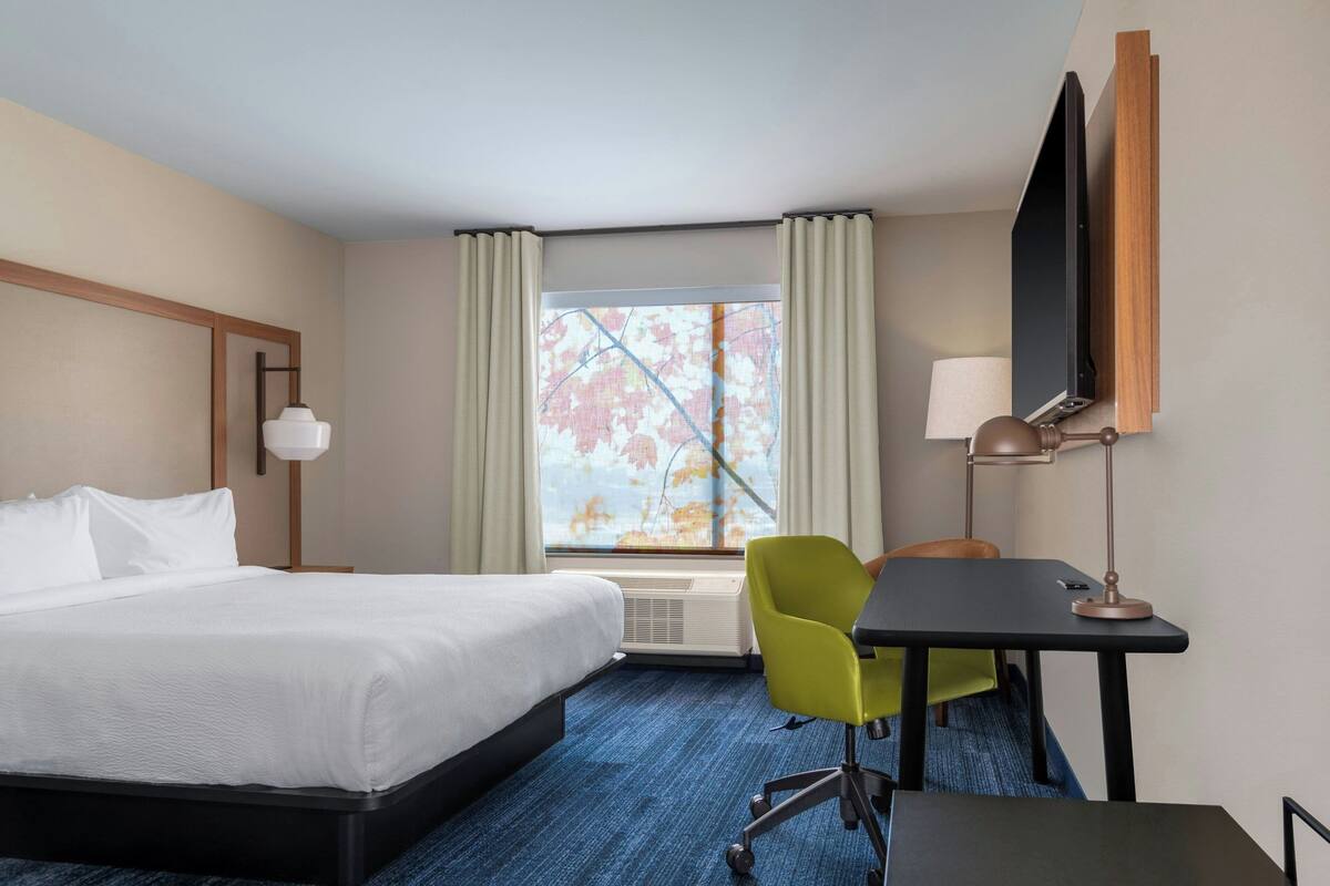 A hotel room with a bed, a desk, a chair, a TV, and a window with curtains.