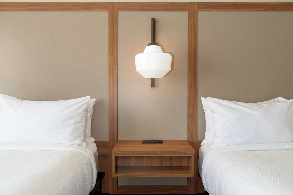 A hotel room with two beds, a nightstand, and a wall-mounted lamp.