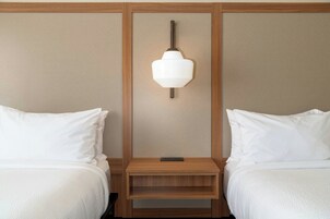 Una habitación de hotel con dos camas, una mesita de noche y una lámpara fijada a la pared.