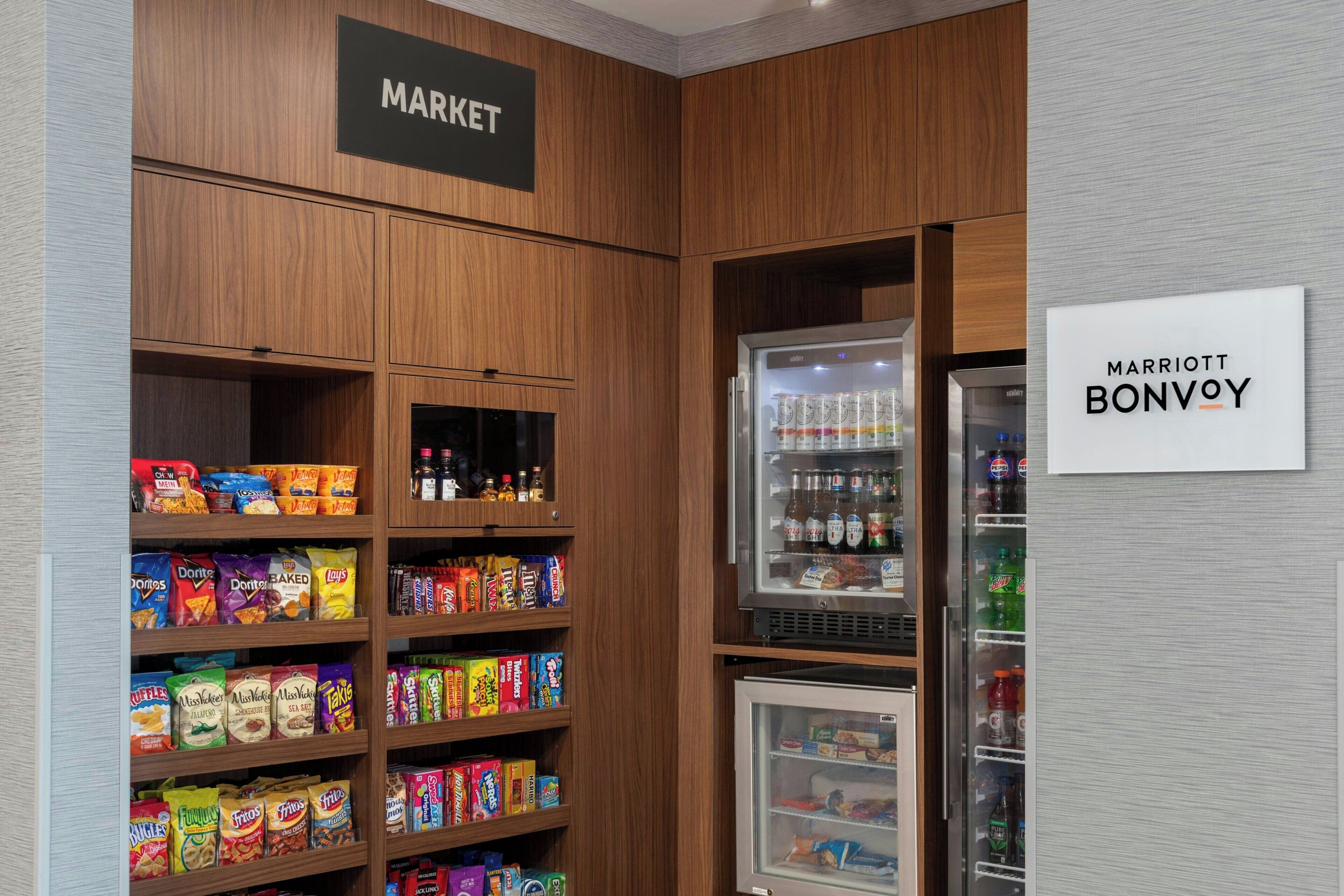 Zona de mercado en un hotel, con estantes llenos de bocadillos y una sección refrigerada con bebidas.