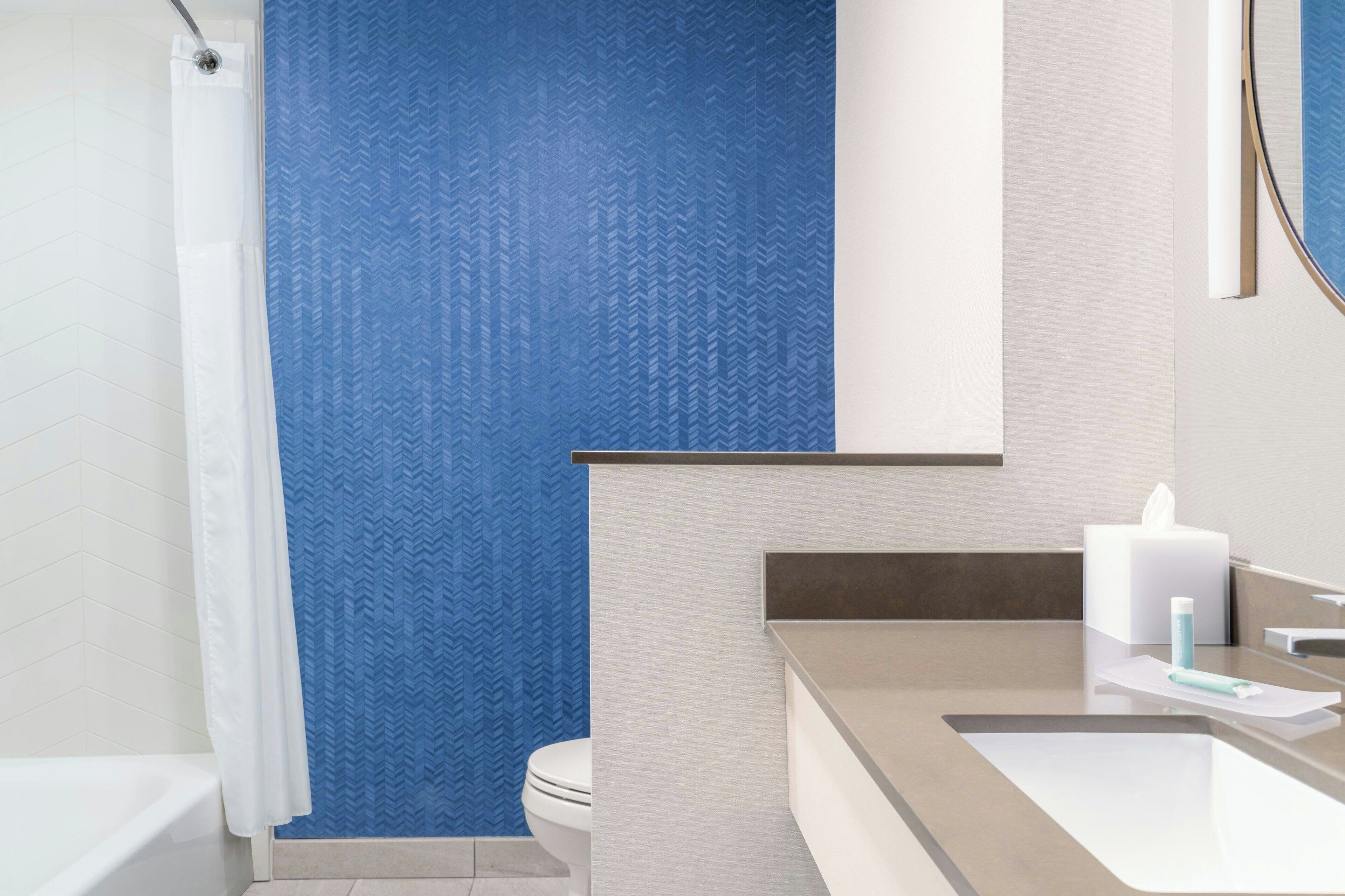 A modern bathroom with a white bathtub, a toilet, and a sink with a towel and tissue box.
