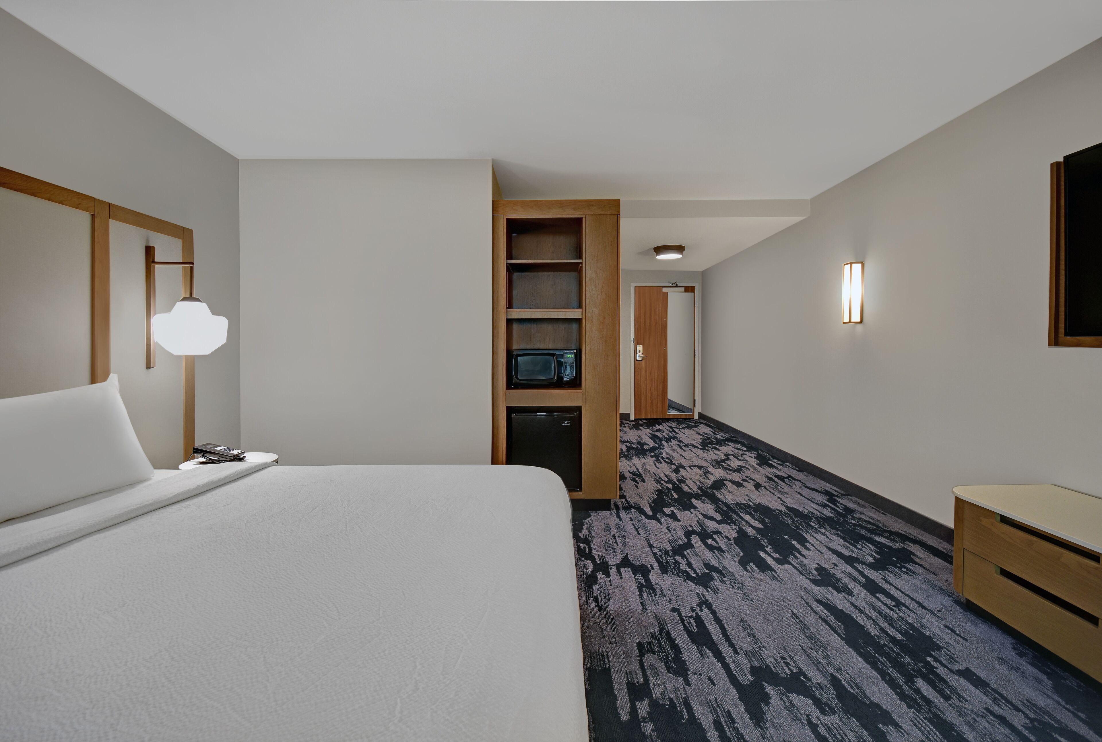 A hotel room with a large bed, a desk, a microwave, a TV, and a wardrobe.