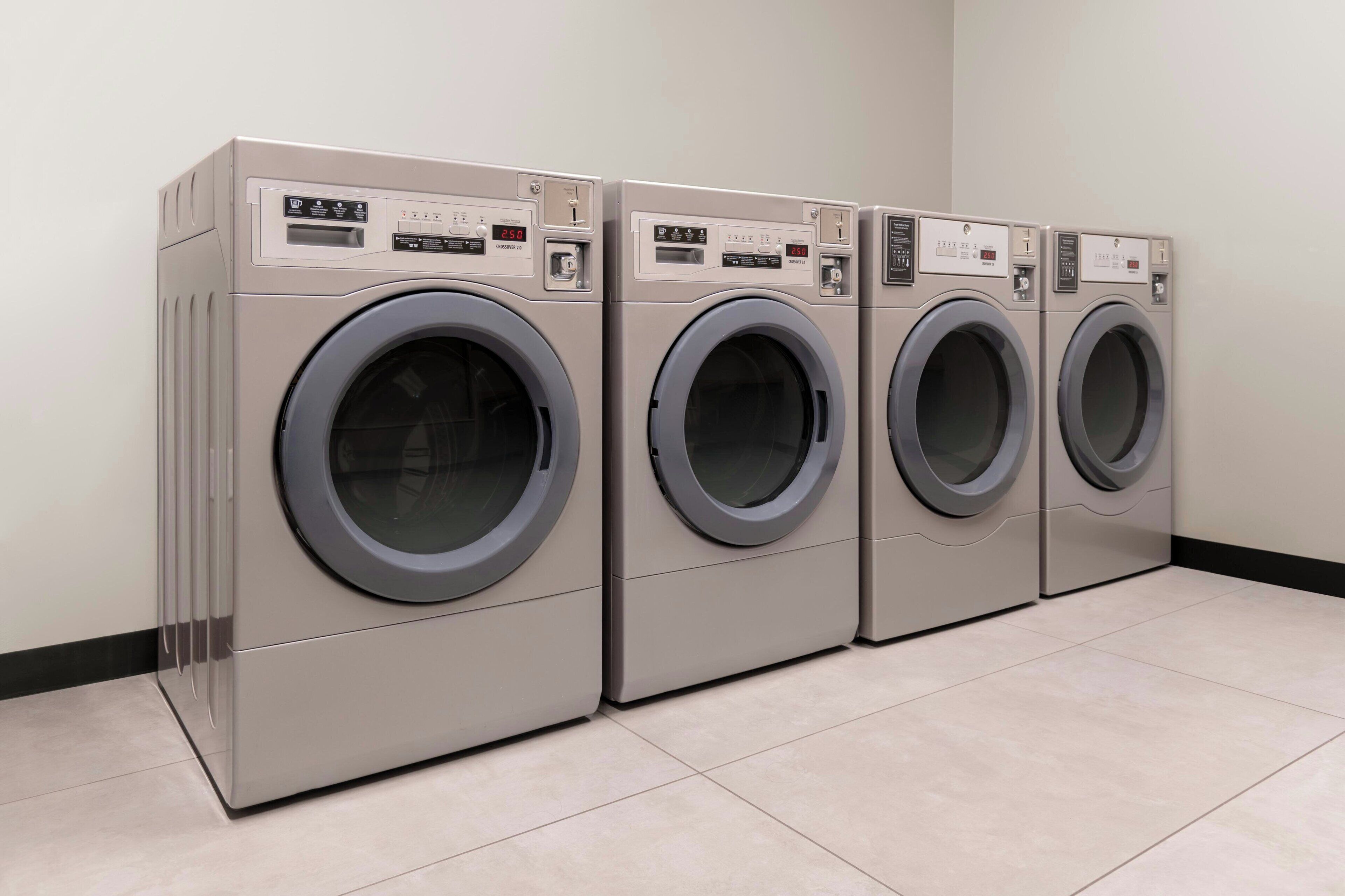 A row of four identical front-loading washing machines in a clean, tiled room.