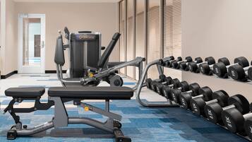 A gym with exercise equipment, including a bench press, a leg press, and a row machine. There are also several sets of dumbbells arranged on a rack.