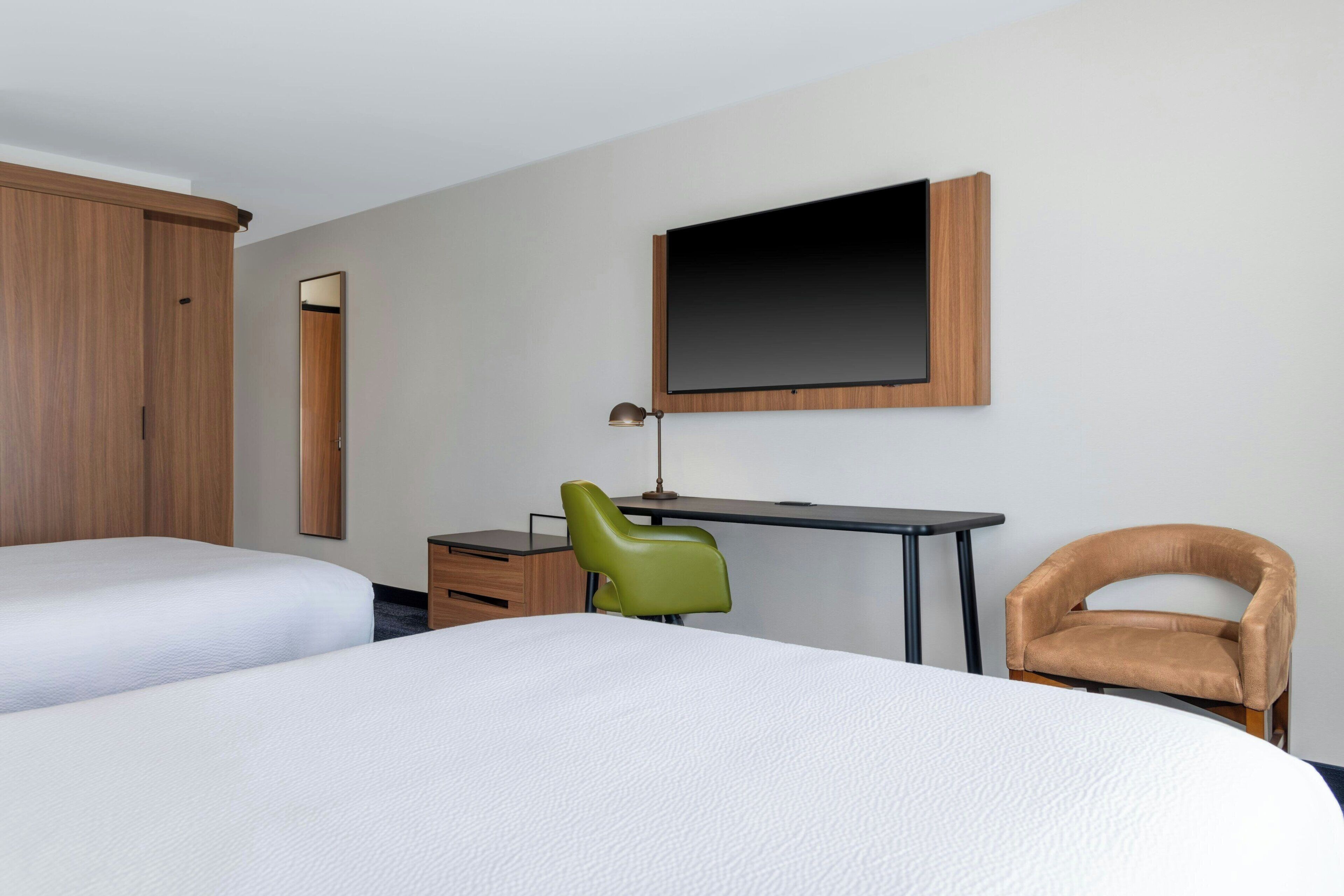 Una habitación de hotel con dos camas, un escritorio, una silla, un televisor y un armario.