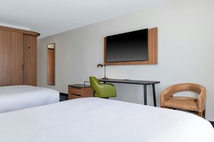 Una habitación de hotel con dos camas, un escritorio, una silla, un televisor y un armario.