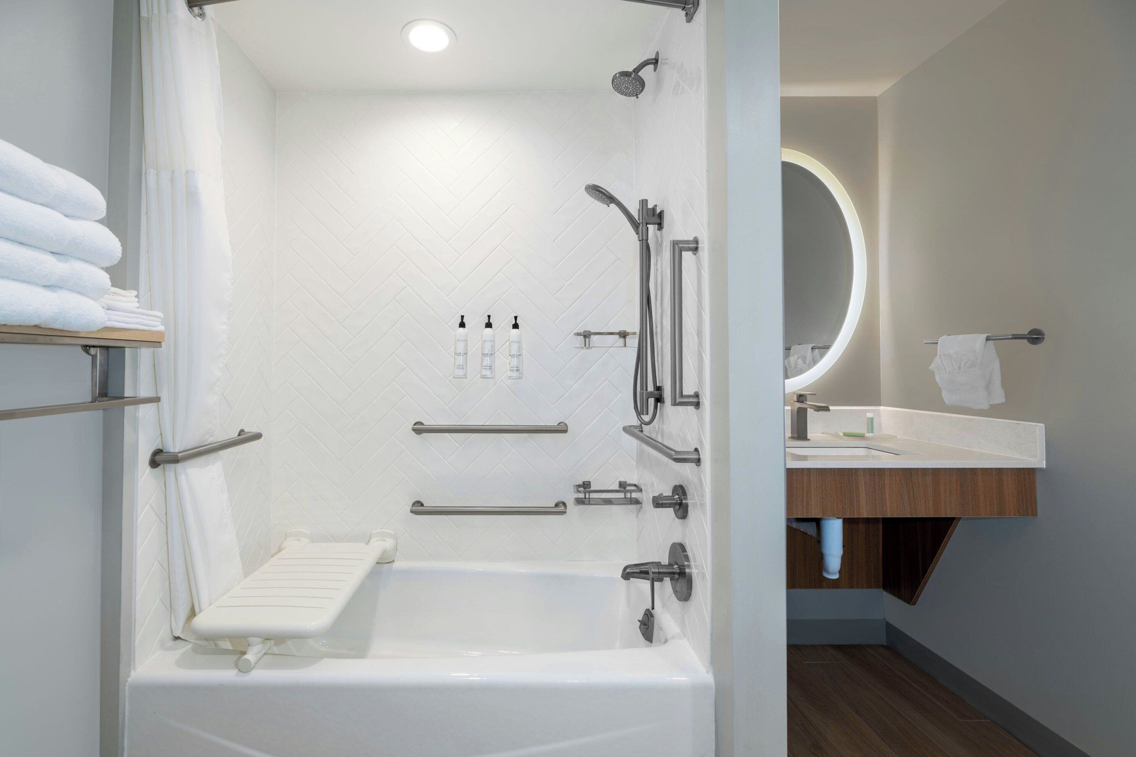 A modern bathroom with a walk-in shower, grab bars, a white bathtub, and a vanity with a mirror.