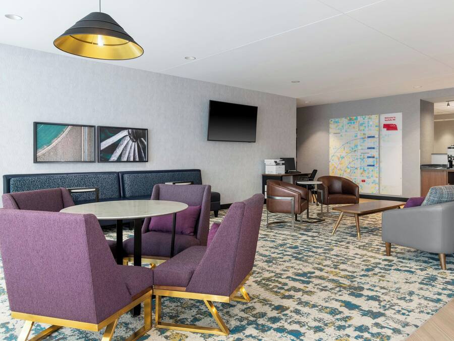 Un vestíbul d'hotel modern amb una taula rodona, cadires morades, un sofà, una televisió i un mapa a la paret.