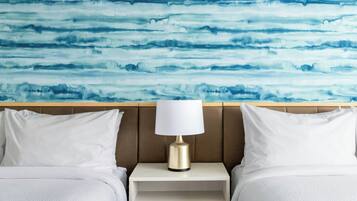 A hotel room with a bed, white pillows, a bedside table with a lamp, and a wall with a blue abstract pattern.