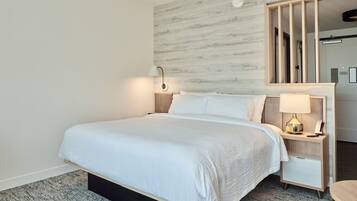 Une chambre d’hôtel moderne avec un grand lit, une table de chevet avec une lampe, un miroir et une petite table.