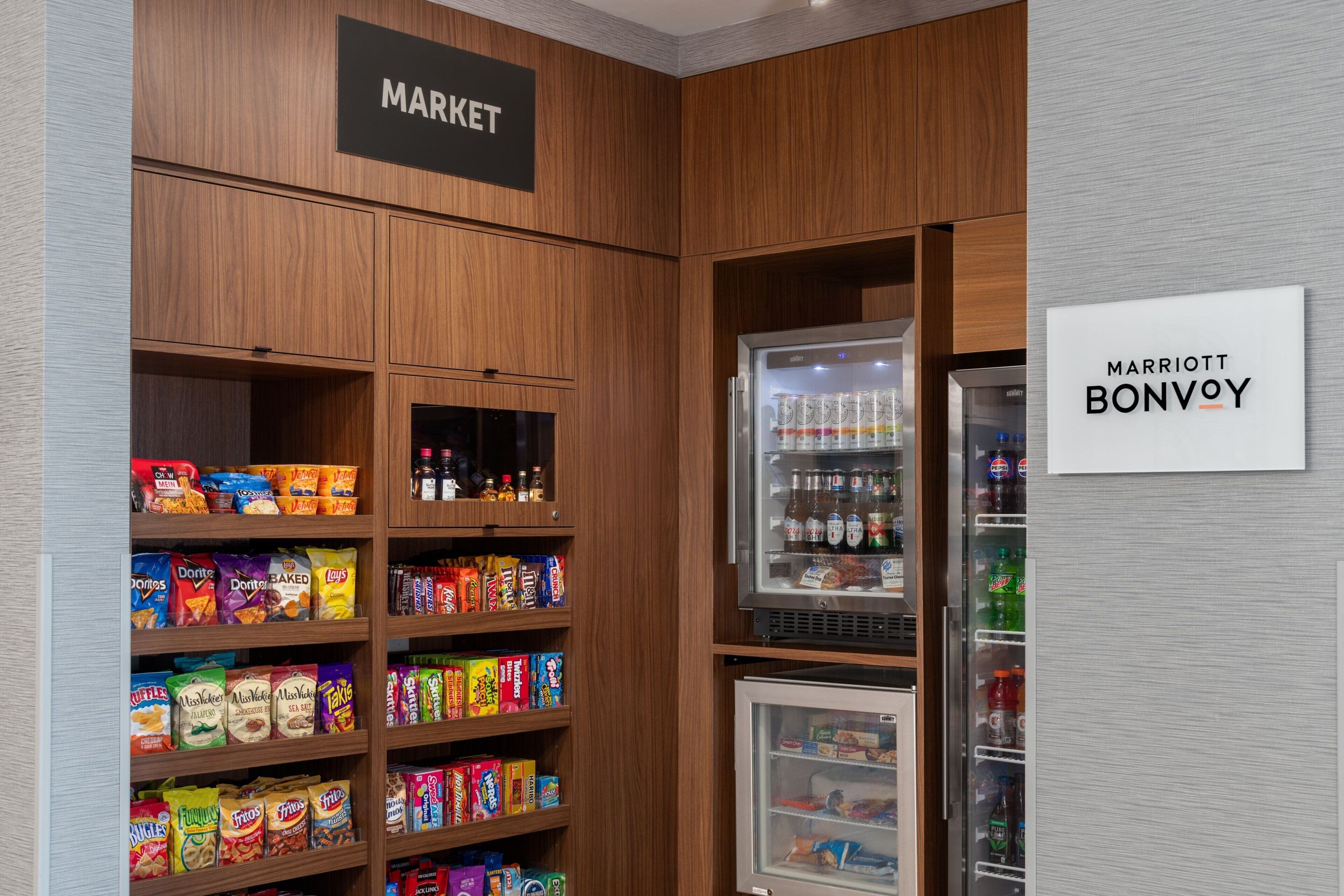 A hotel market area with shelves stocked with snacks and a refrigerated section with beverages.
