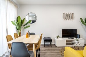 Una sala de estar moderna con una mesa de comedor, sillas, un televisor y decoración en la pared.