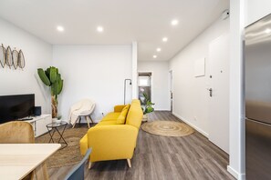 Un salon moderne avec un canapé jaune, un téléviseur, une plante et un coin repas.