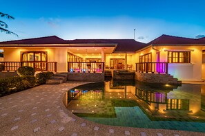 Una casa de dos pisos con piscina, un patio techado y fachada bien iluminada.