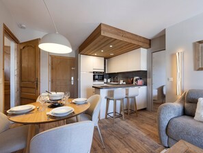 A modern kitchen with wooden beams, a dining area with a round table and bar stools, and a cozy seating area with a sofa.