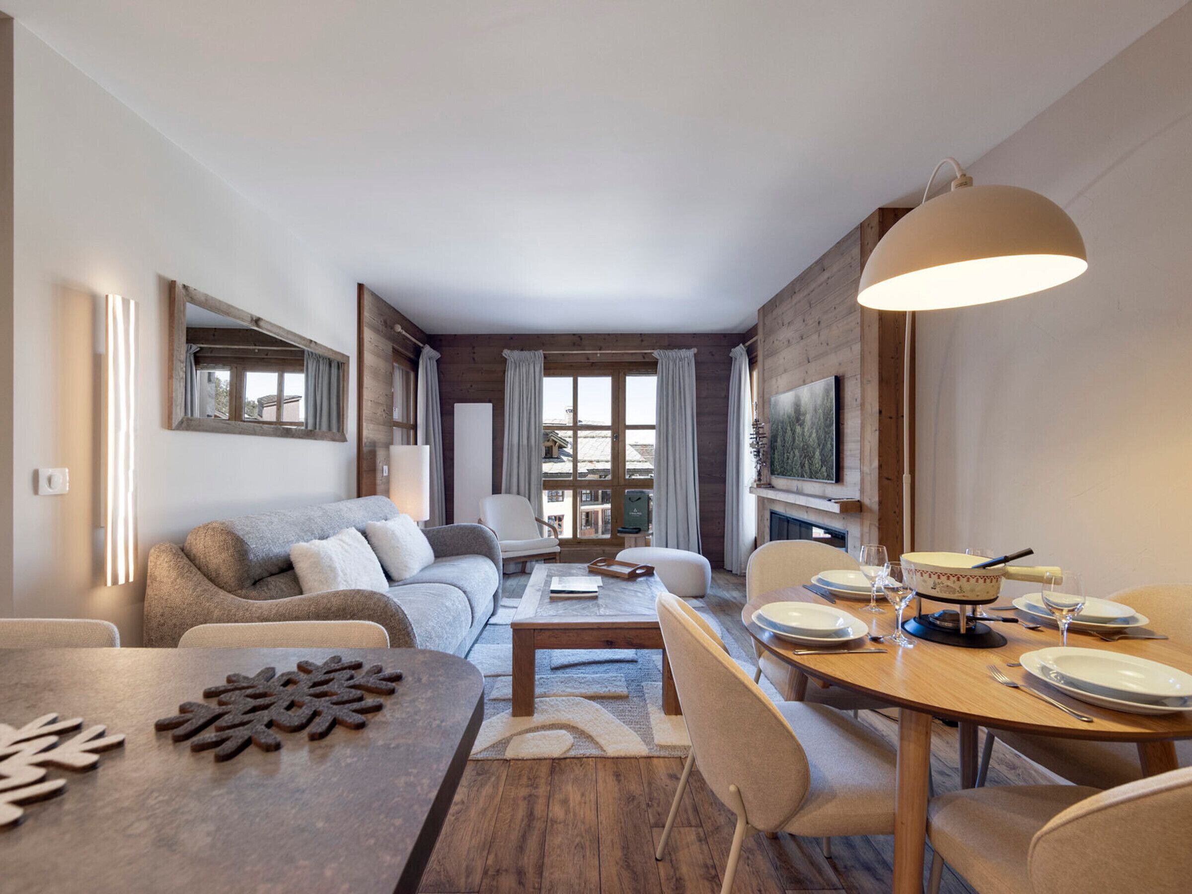 A modern living room with a sofa, dining table, and chairs. There is a fireplace and a television mounted on the wall.