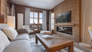 Una sala de estar acogedora con detalles de madera, una chimenea, un televisor grande y vistas a través de las ventanas.