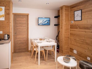 Una habitación acogedora con paredes de madera, una mesa blanca preparada para cuatro personas y un cuadro de un paisaje montañoso.