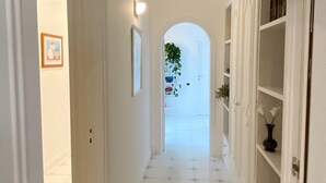 Um corredor com paredes brancas, piso de azulejos e uma porta que dá para outro cômodo.
