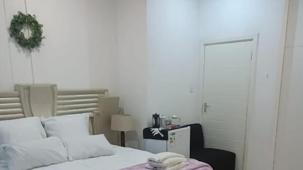 A hotel room with a bed, a nightstand, a coffee machine, a door, and a small table with a flower. - Danodeb Lodge  (Pietermaritzburg)