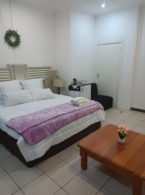 A hotel room with a bed, a nightstand, a coffee machine, a door, and a small table with a flower. - Danodeb Lodge  (Pietermaritzburg)