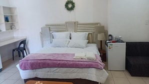A neatly arranged bedroom with a bed, bedside tables, a desk, and a small refrigerator. - Danodeb Lodge  (Pietermaritzburg)