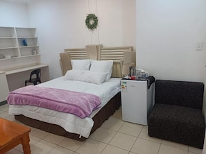 A bedroom with a bed, a small refrigerator, a desk, a chair, and a couch.