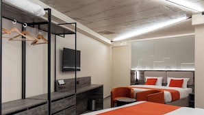 Quarto de hotel moderno com uma cama, duas cadeiras, uma escrivaninha e uma televisão.