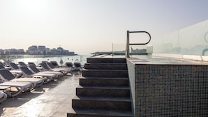 Área de piscina no terraço com espreguiçadeiras e vista para o horizonte da cidade.