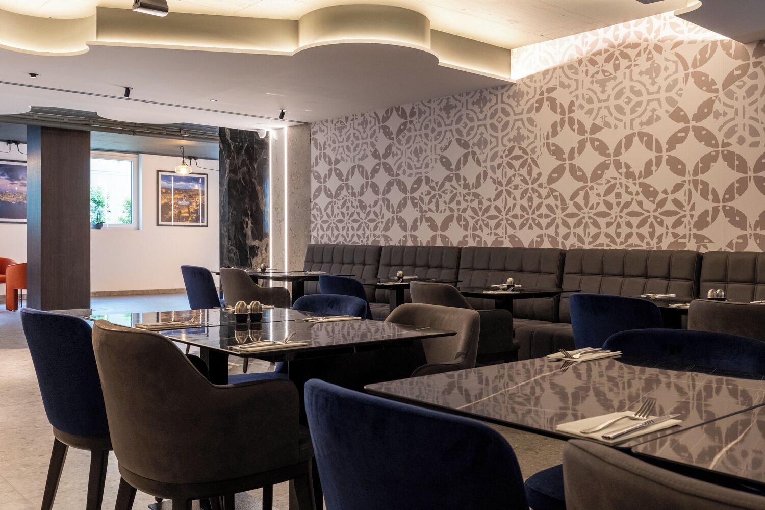 Um restaurante moderno com cabines e mesas em tons escuros, parede com padrão e uma janela ampla com vista.