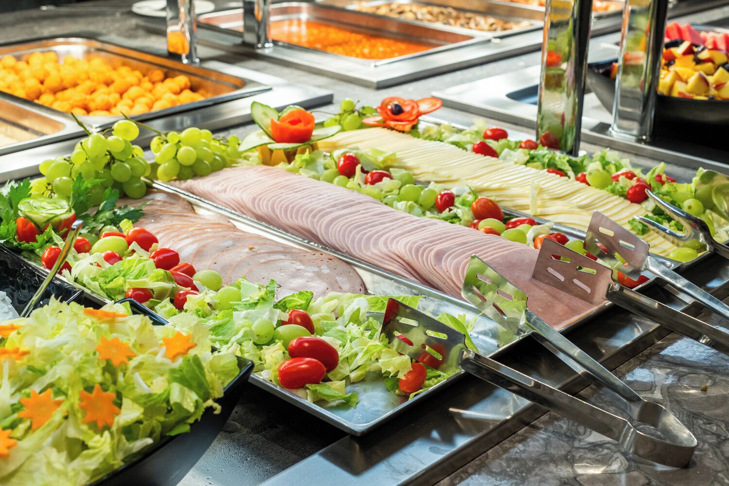 A buffet with various food items including sliced meats, salads, and fruits.