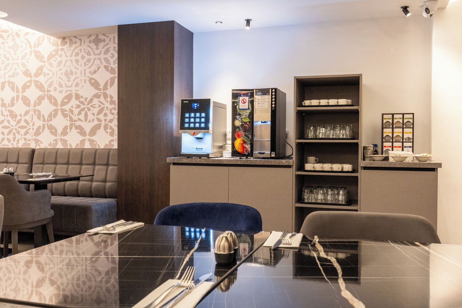 A modern hotel room with a dining area, a minibar, and a coffee machine.