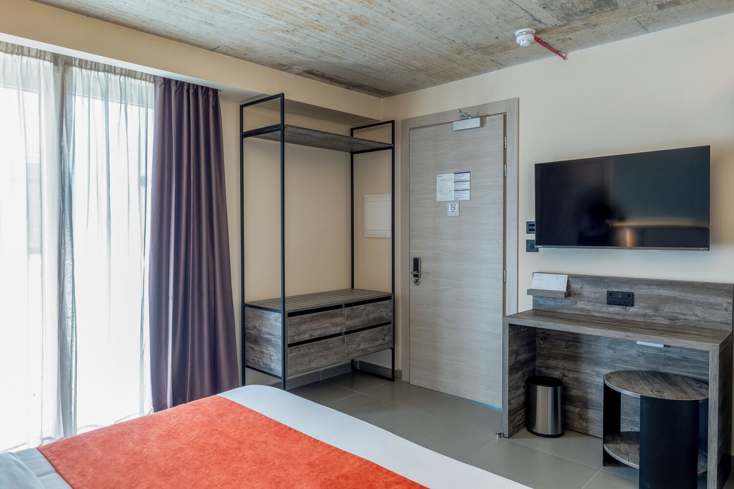 Una habitación de hotel moderna con cama, escritorio, televisor y armario.