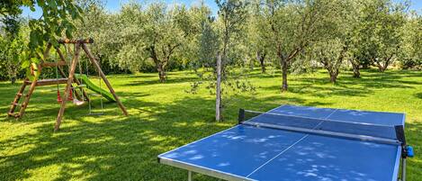 A ping pong table in a grassy outdoor area with a swing set and trees in the background.