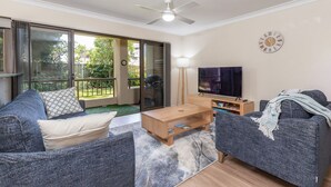 A living room with a sofa, coffee table, and TV. There is a sliding glass door leading to a balcony. - Wallis Gardens 11 - short stroll to beautiful Wallis lake (Forster)