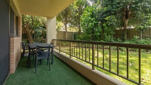 A covered patio with a table and chairs, surrounded by a metal railing and greenery. - Wallis Gardens 11 - short stroll to beautiful Wallis lake (Forster)