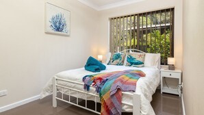 A bedroom with a bed, a nightstand, a window with blinds, and a wall-mounted artwork. - Wallis Gardens 11 - short stroll to beautiful Wallis lake (Forster)