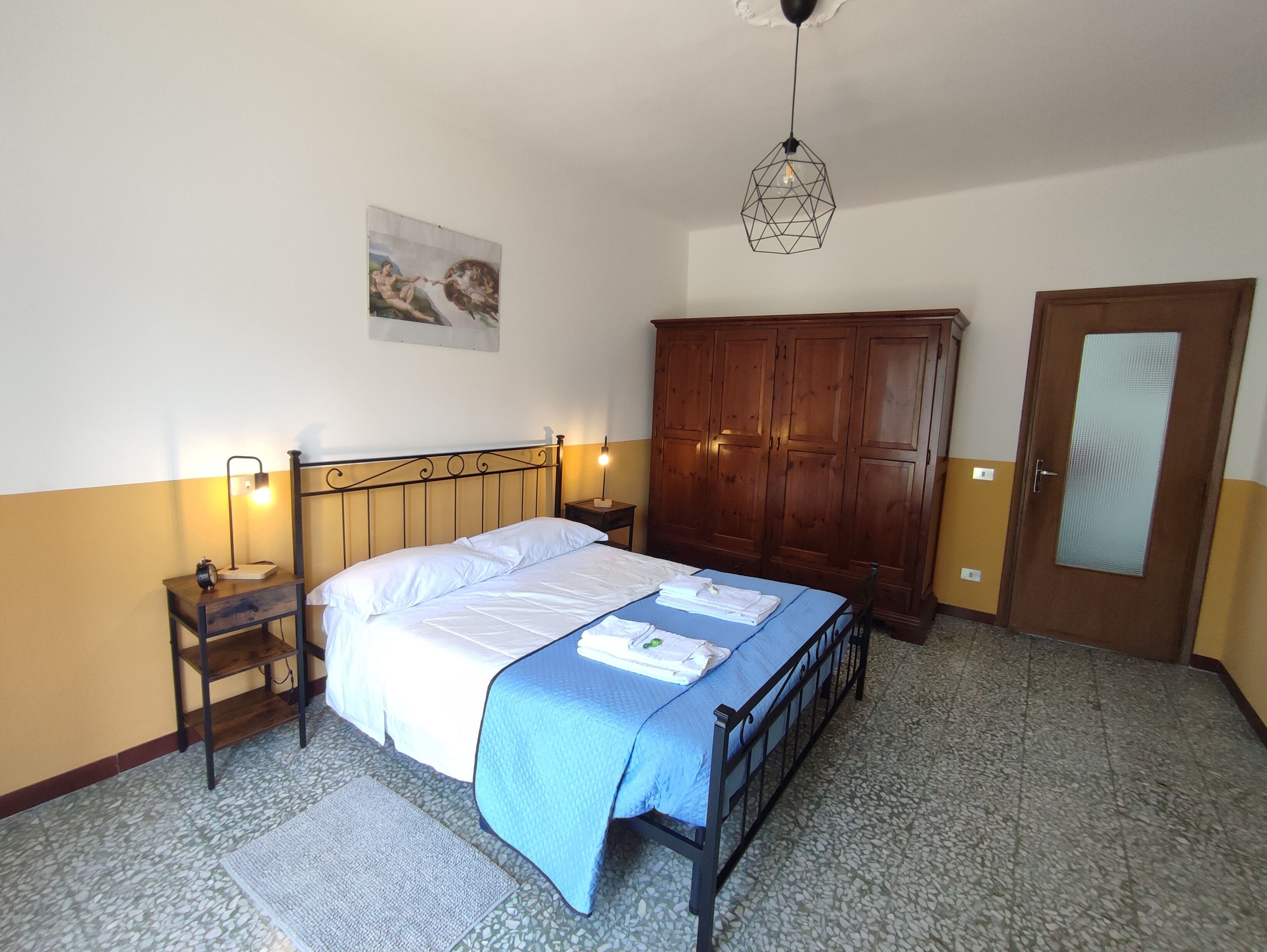 A bedroom with a bed, a wardrobe, a nightstand, a lamp, and a painting on the wall.