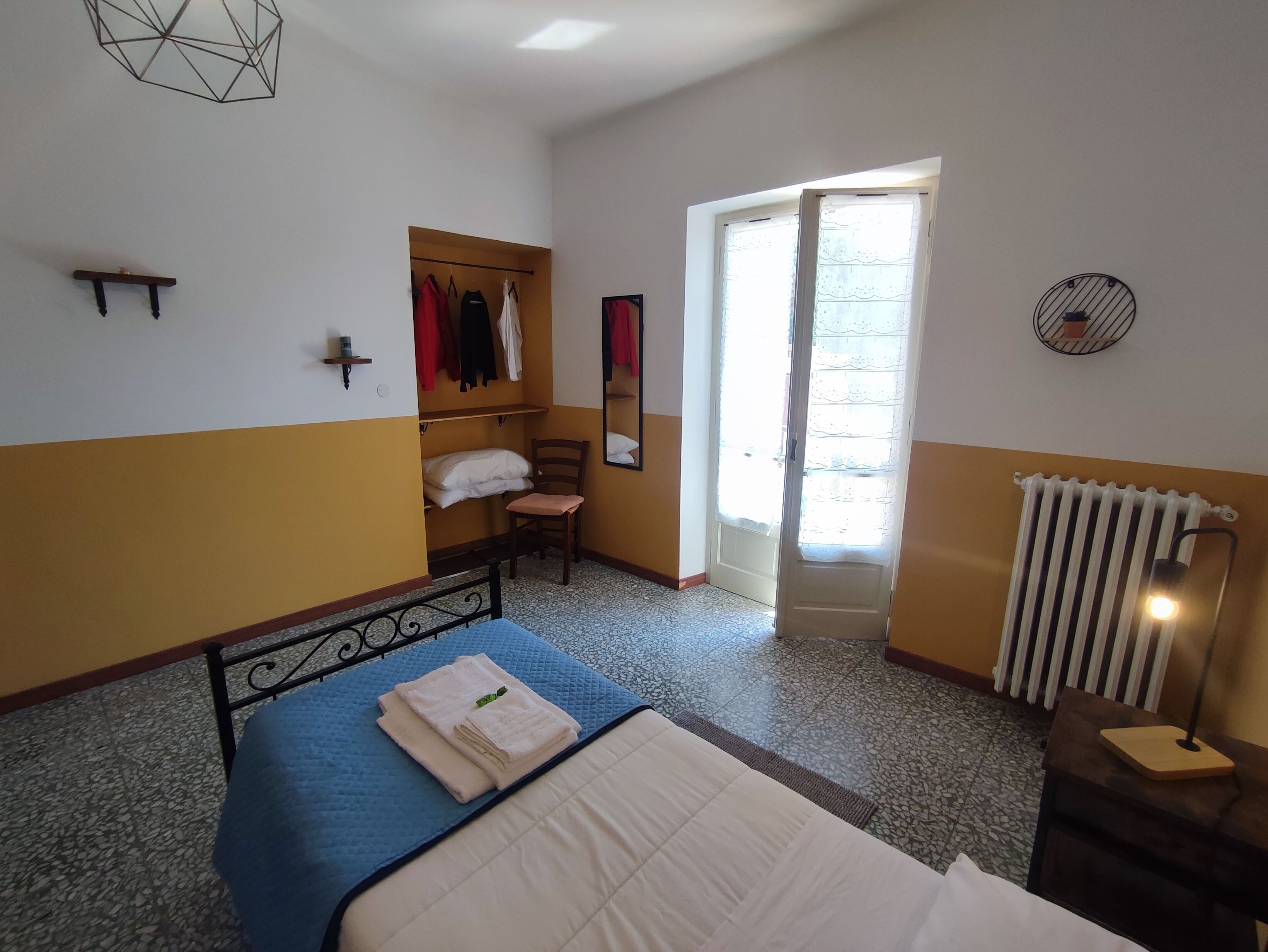 A bedroom with a bed, a chair, a wardrobe, a radiator, and a window.