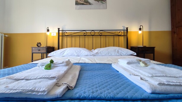 A double bed with white linens and a blue quilt, two bedside tables with lamps, a wall clock, and a painting above the bed. - Michelangelo - spacious apartment with view in La Morra  (Piemonte)