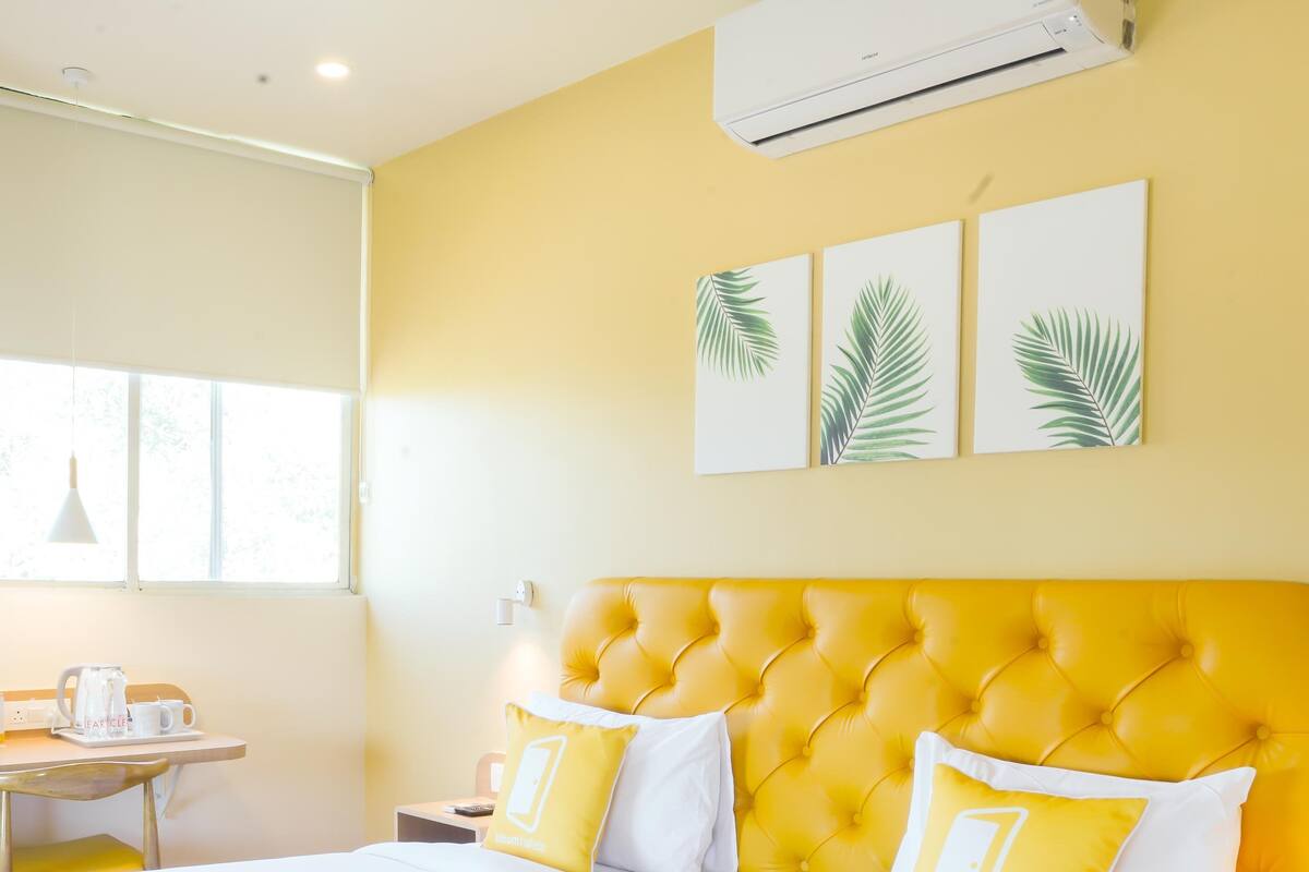 Une chambre d’hôtel avec deux lits, une tête de lit jaune, du linge de lit blanc et une fenêtre laissant entrer la lumière naturelle.