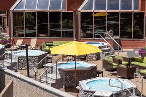 An outdoor pool area with hot tubs, lounge chairs, and umbrellas.