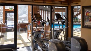 Une salle de sport équipée de tapis de course et dotée d’un espace piscine visible à travers des portes vitrées.