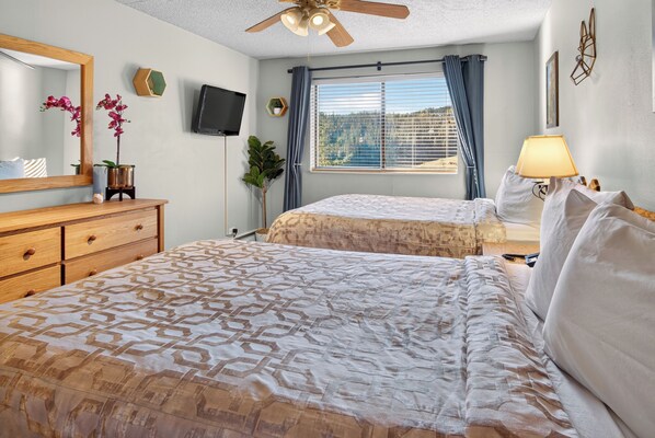 A hotel room with two beds, a ceiling fan, a TV, and a window with curtains.