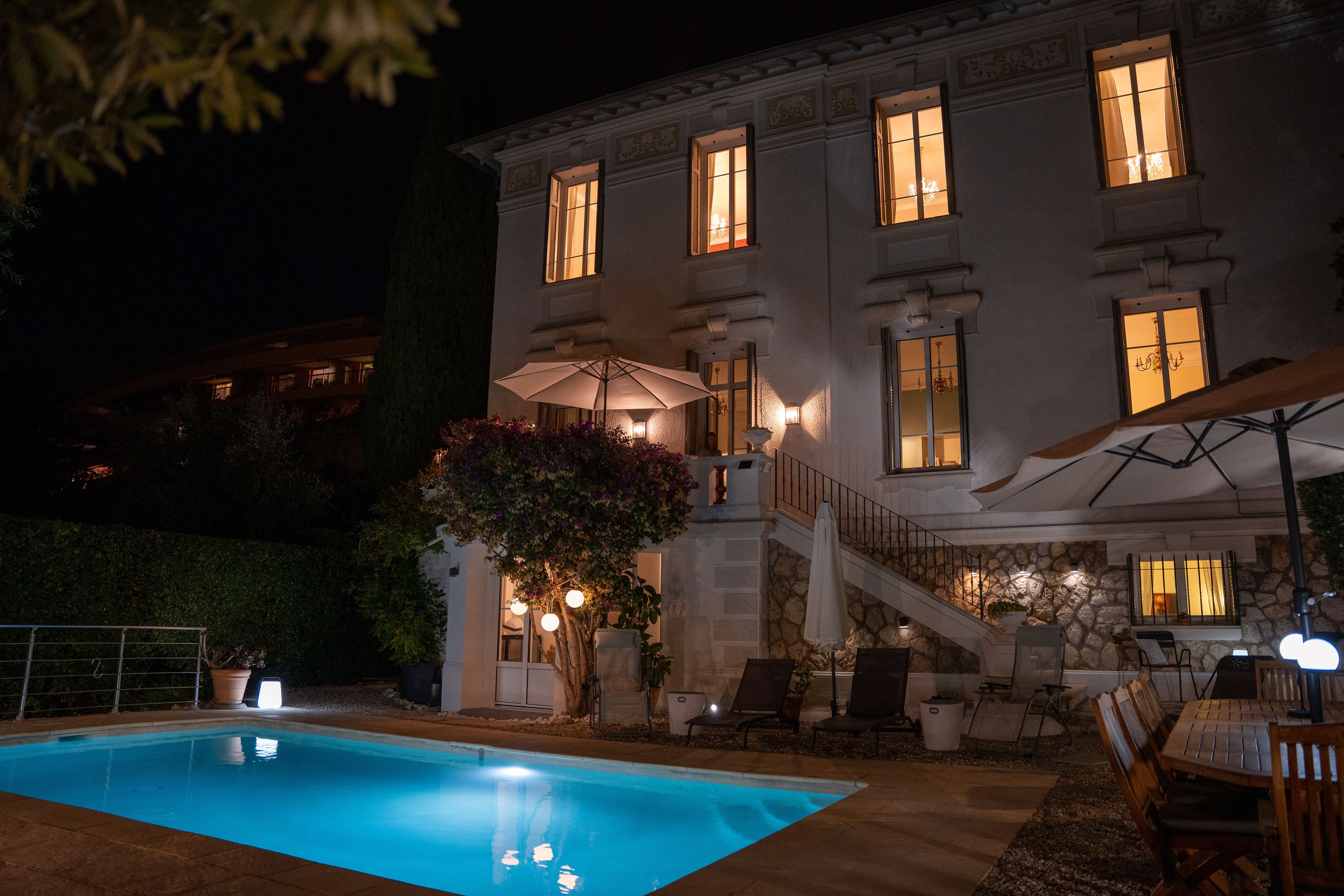 A nighttime view of a building with a swimming pool, outdoor seating, and illuminated windows.