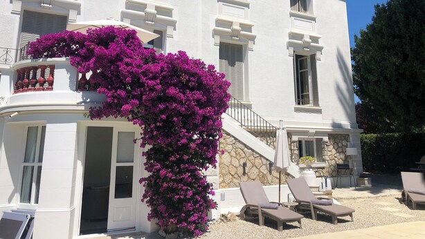 A white building with a stone facade, a balcony with purple flowers, and outdoor seating with umbrellas. - Stunning Belle Epoque Villa in the heart of Cannes, private pool, secure parking (Cannes)