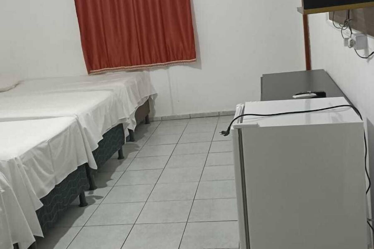 Ein Zimmer mit zwei Betten, die mit weißen Laken bezogen sind, einem roten Vorhang, einem weißen Schrank und einem gefliesten Boden.